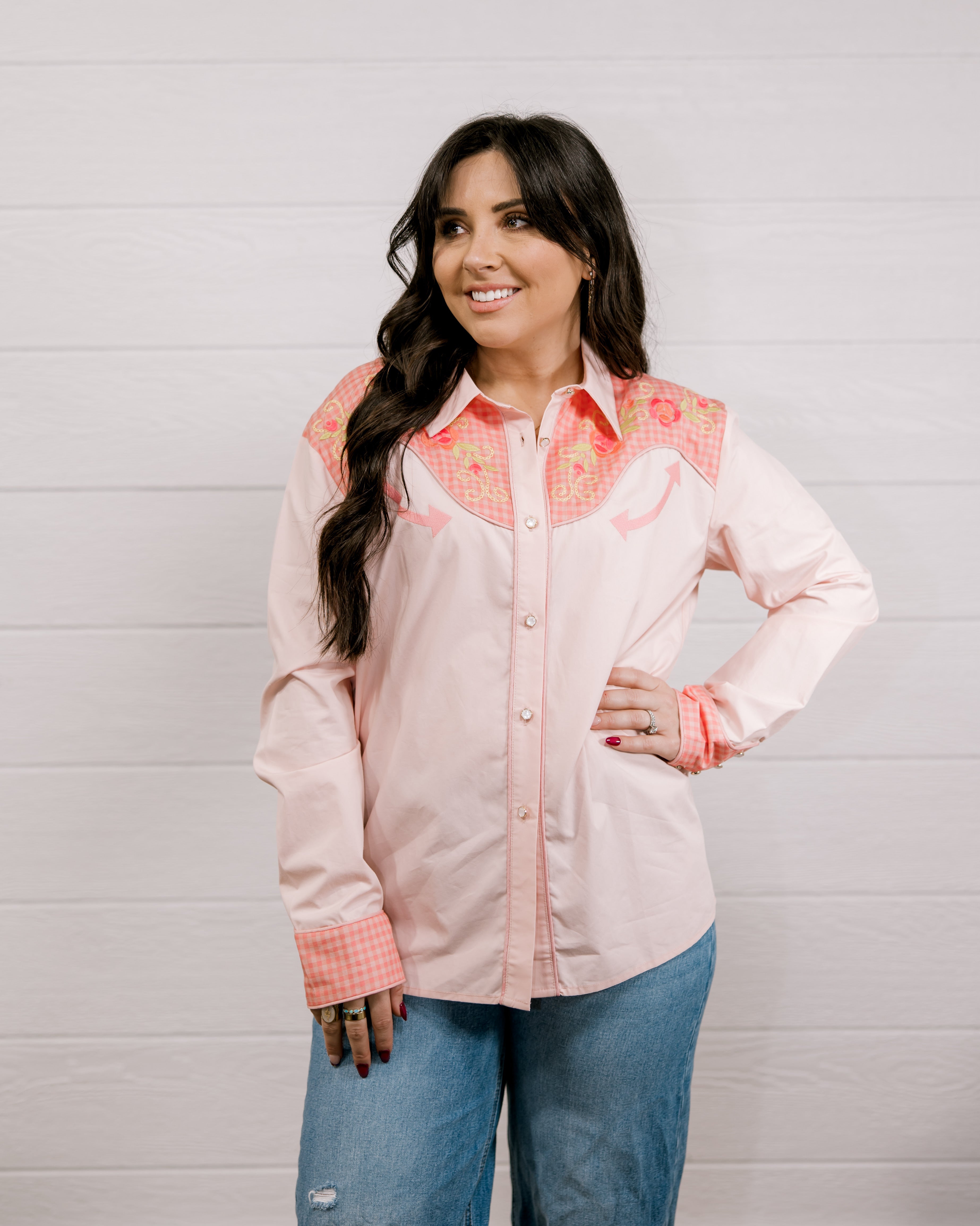 Woman wearing a light pink shirt western shirt with coral & green accents against a white background