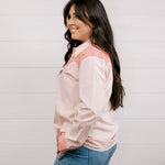 Side view of woman wearing a light pink shirt western shirt with coral & green accents against a white background