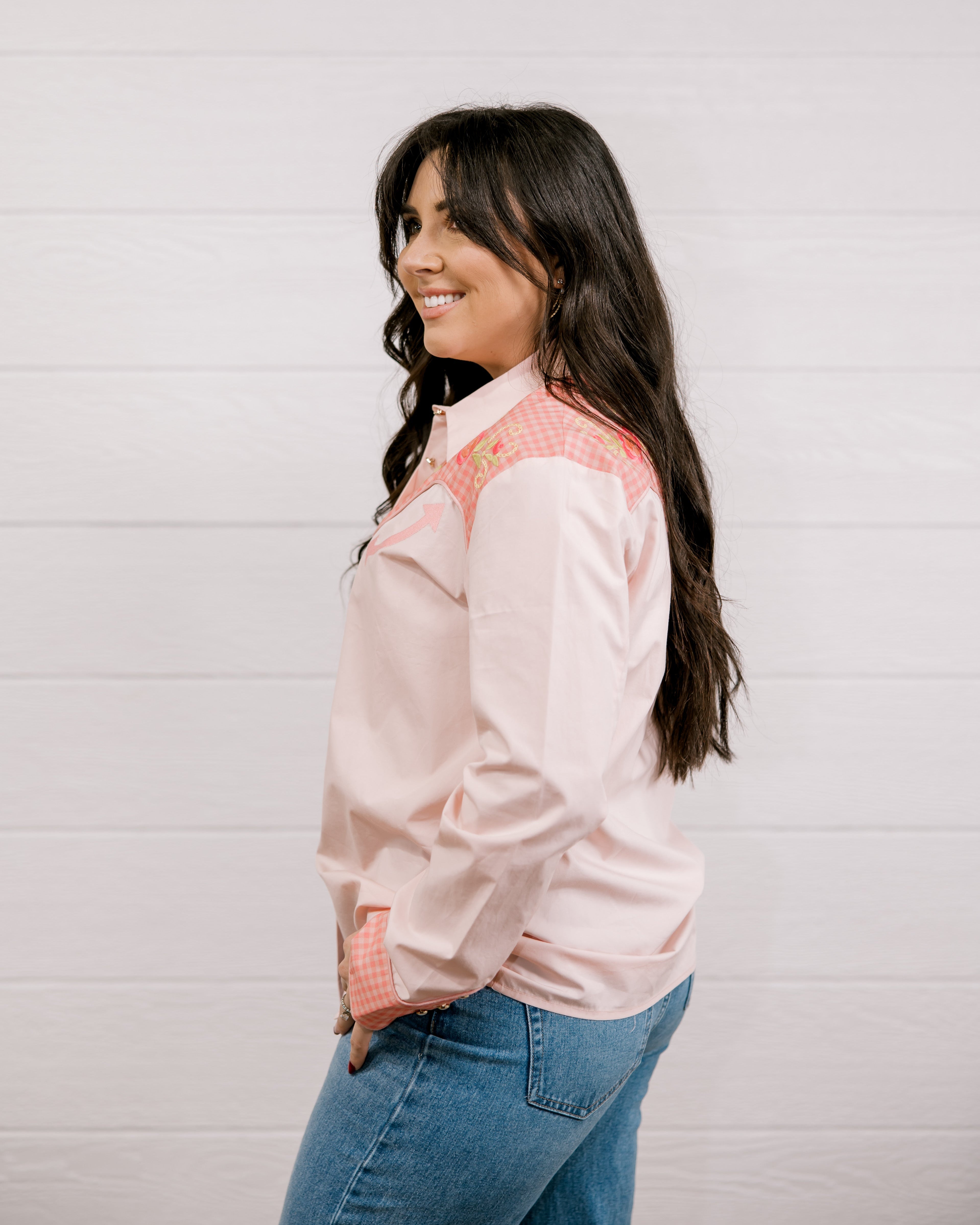 Side view of woman wearing a light pink shirt western shirt with coral & green accents against a white background