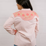 Back view of women wearing a light pink shirt western shirt with coral & green accents against a white background
