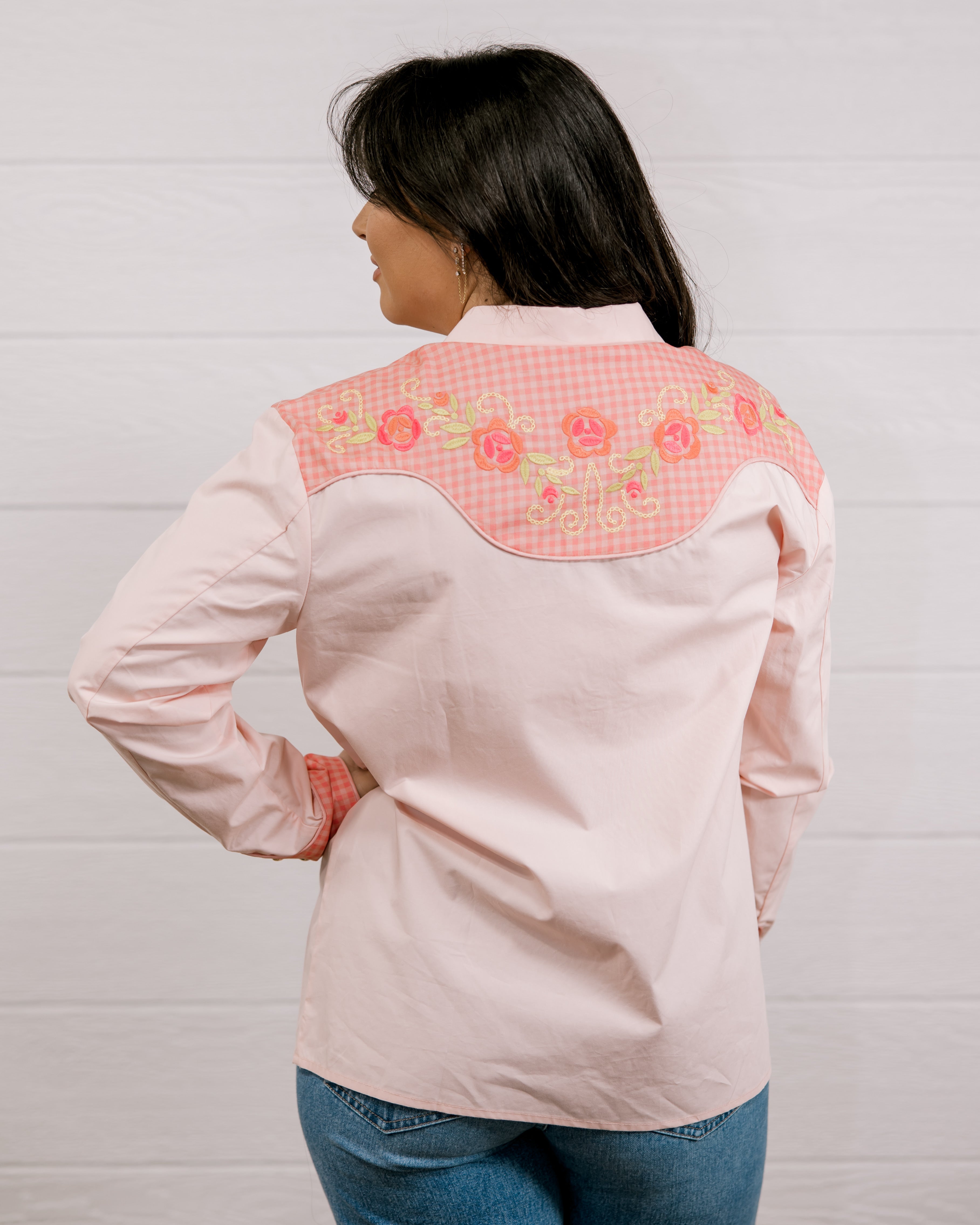 Back view of women wearing a light pink shirt western shirt with coral & green accents against a white background