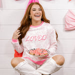 Woman in a 'LOVED' pajama set holding cookies, sitting on a chair with pink decorations.