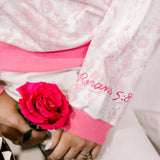 Close-up of a person wearing a white jacket with pink floral patterns and a pink rose, on a checkered floor.