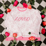 White sweatshirt with pink text on a checkered background with flowers