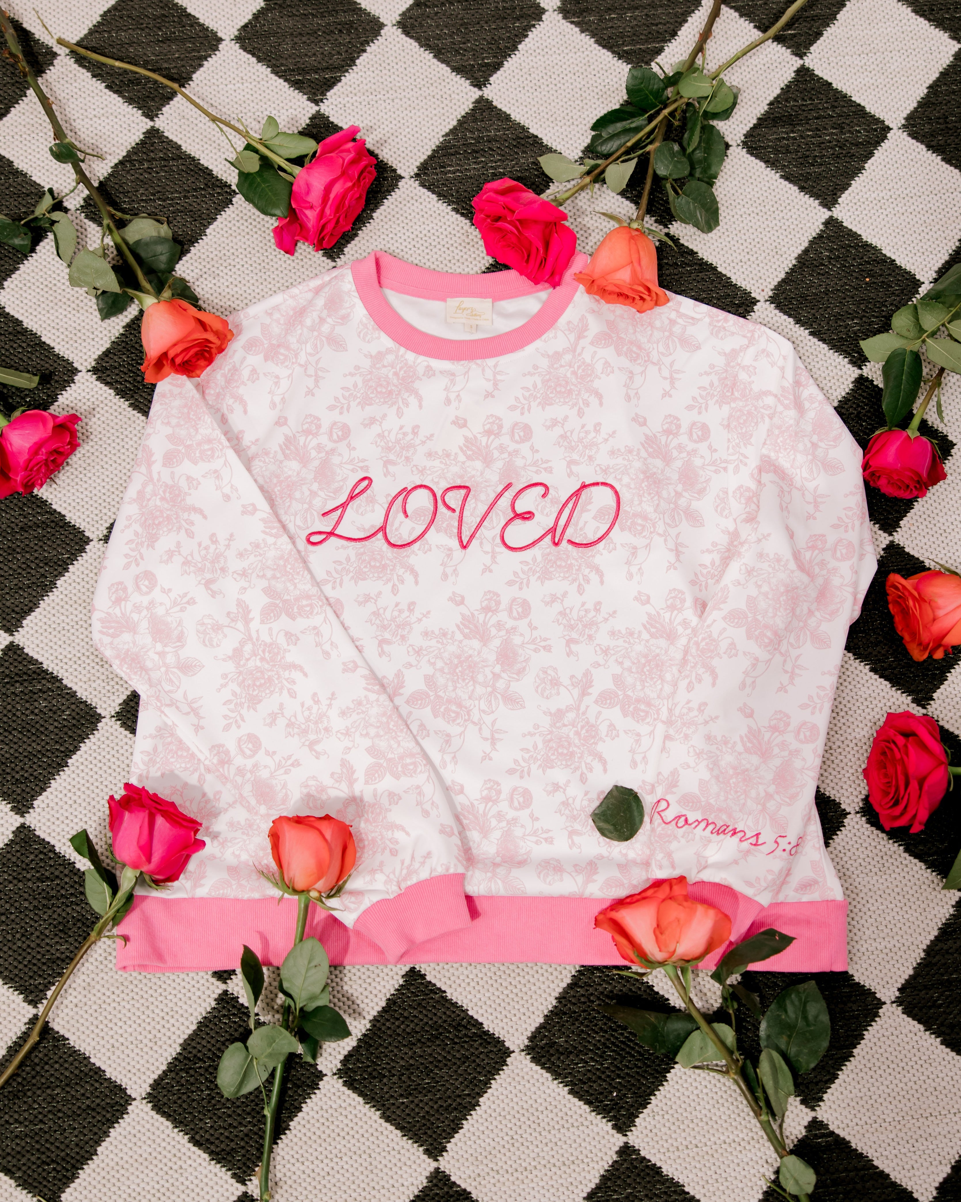 White sweatshirt with pink text on a checkered background with flowers