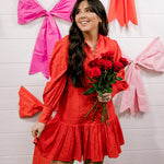 Woman wearing a red eyelet dress standing against a white wall.