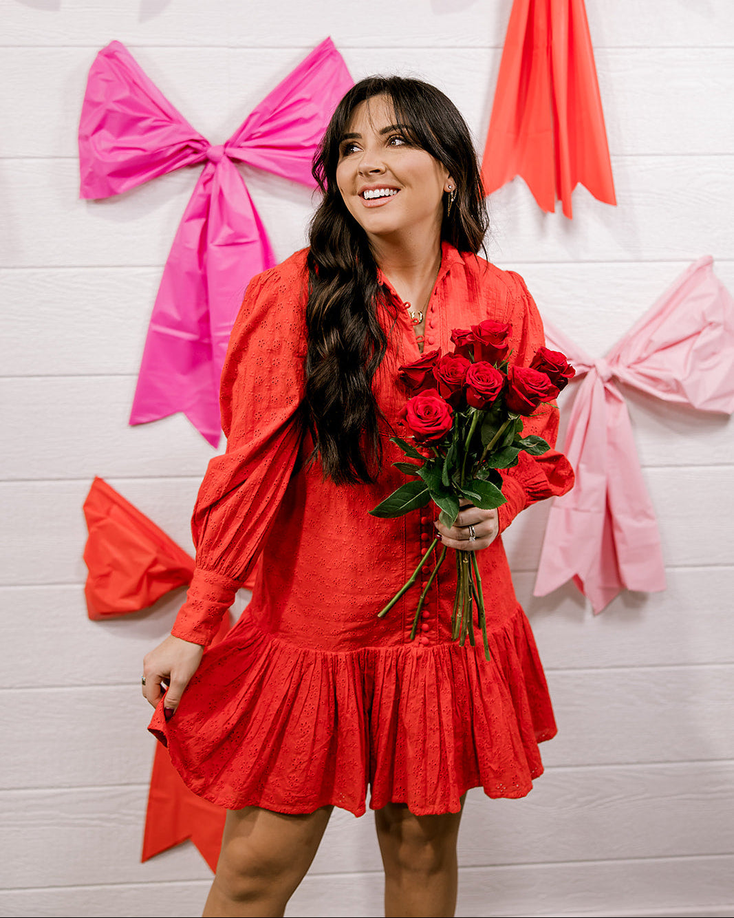 Woman wearing a red eyelet dress standing against a white wall.