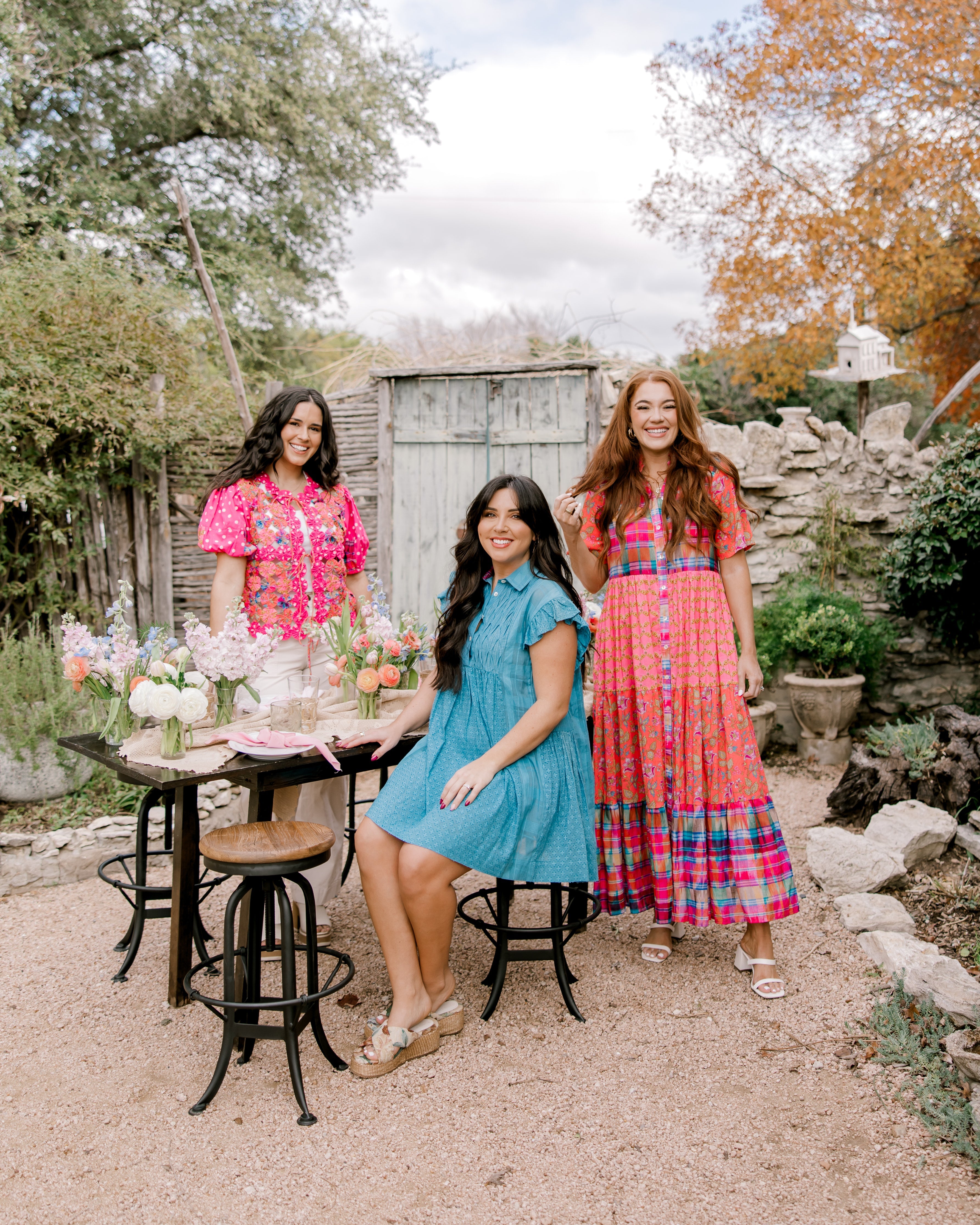 Women in bright colored outfits in a garden having a tea party. 