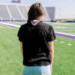 Woman with dark hair wearing a short-sleeve black eyelet pattern top, and a light-wash denim skirt. 