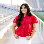 Model with dark hair facing forward wearing a short-sleeve red eyelet top and a white denim skirt. 