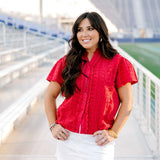 Model with dark hair facing forward wearing a short-sleeve red eyelet top and a white denim skirt. 