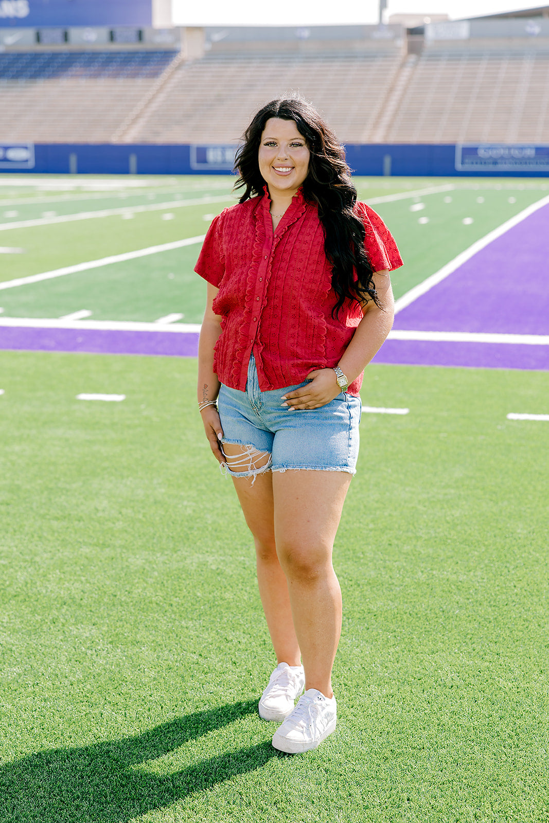Model facing to the side wearing a short-sleeve red top with eyelet pattern and light-wash denim shorts. 