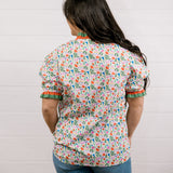A women wearing a floral top with green and red trim with a ruffle collar and sleeves showing the back