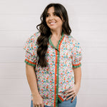 A women wearing a floral top with green and red trim with a ruffle collar and sleeves showing the front 