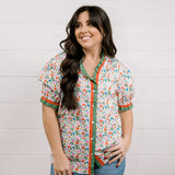 A women wearing a floral top with green and red trim with a ruffle collar and sleeves showing the front 