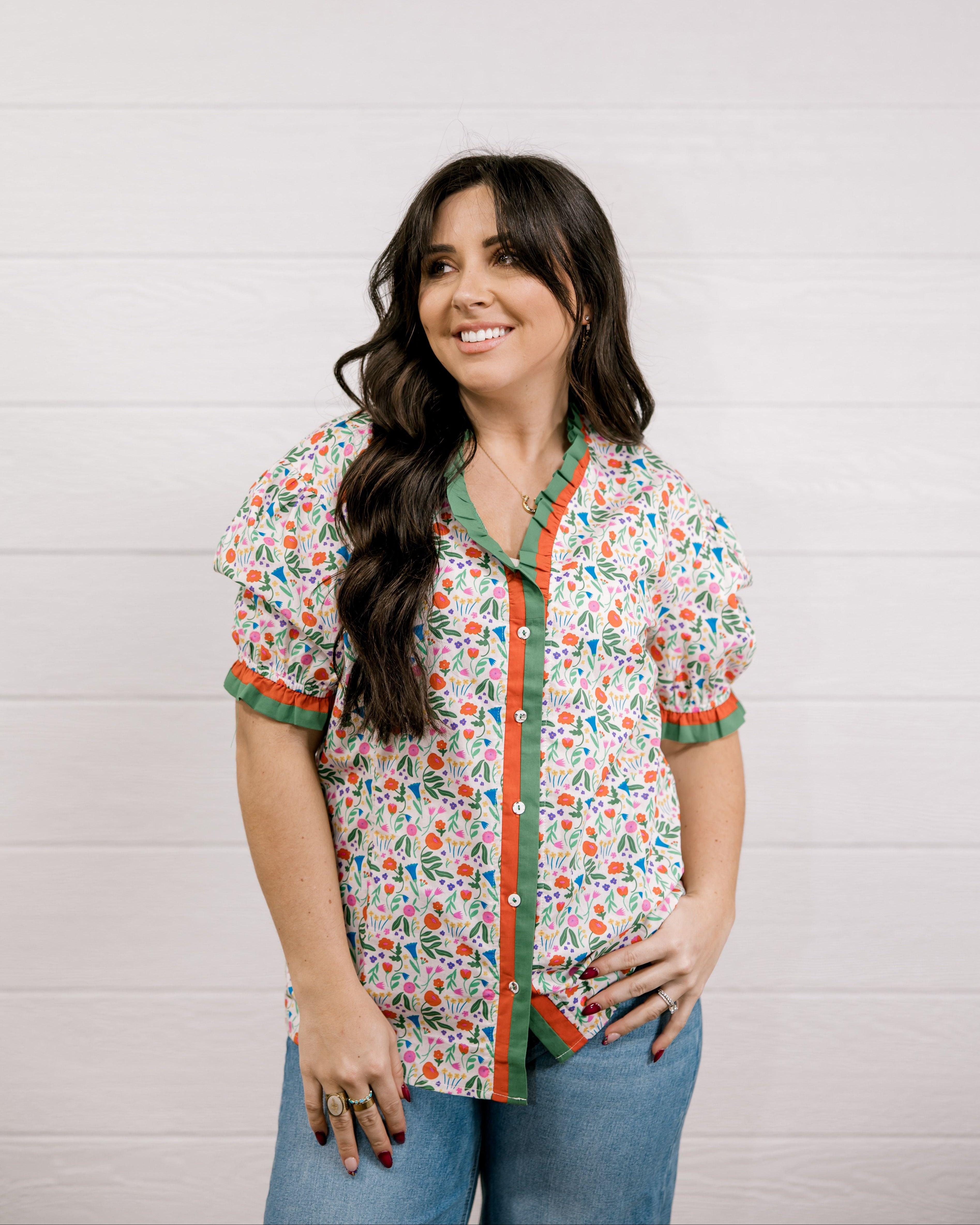 A women wearing a floral top with green and red trim with a ruffle collar and sleeves showing the front 