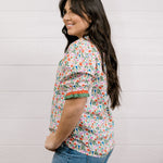 A women wearing a floral top with green and red trim with a ruffle collar and sleeves showing the side and sleeve