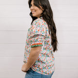A women wearing a floral top with green and red trim with a ruffle collar and sleeves showing the side and sleeve