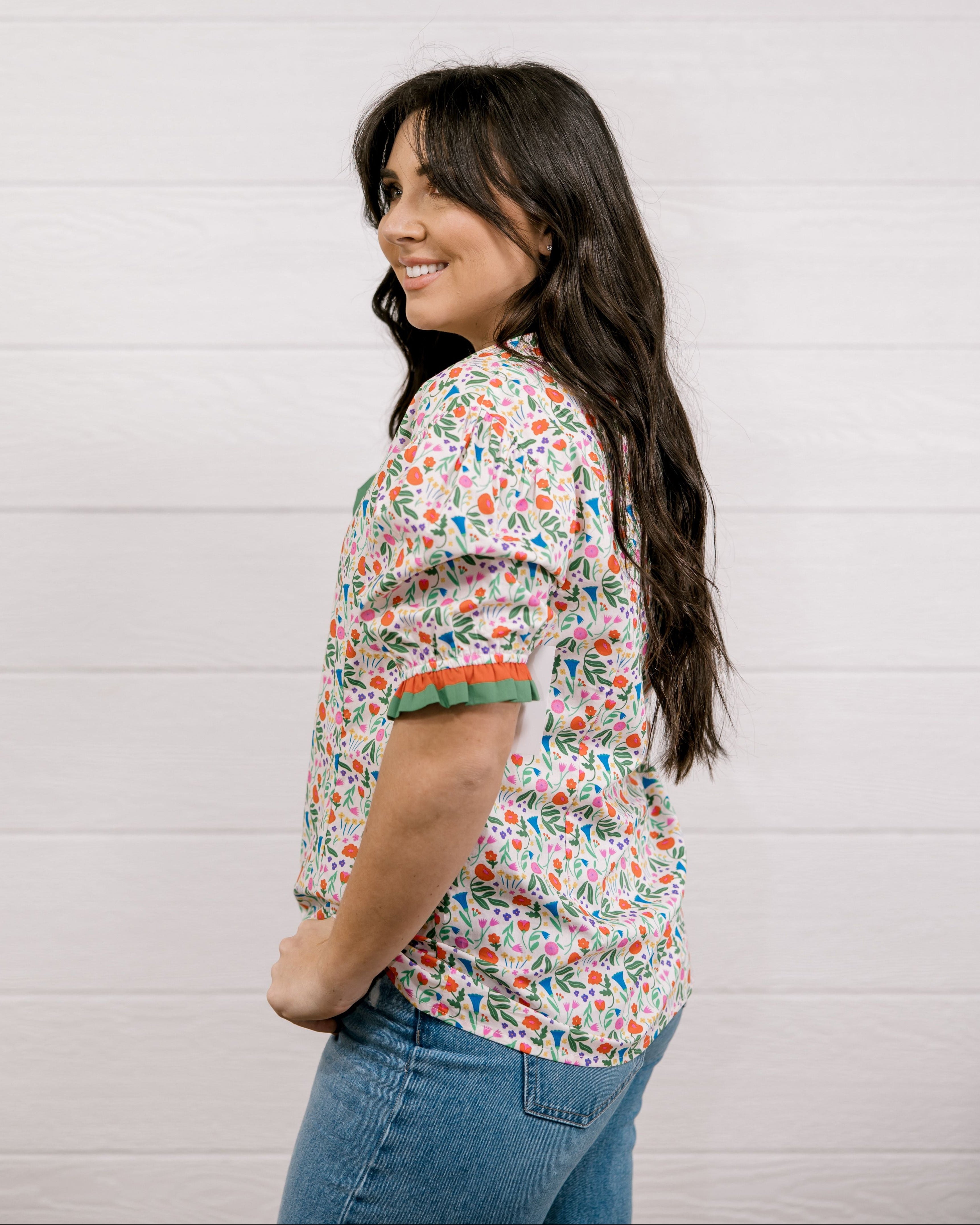 A women wearing a floral top with green and red trim with a ruffle collar and sleeves showing the side and sleeve