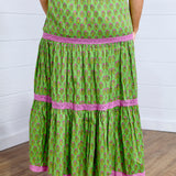 Model in a back profile position against a white background in the Madison Maxi Skirt. The image portrays length of skirt, the embroidery, and graphics on back of skirt. Model paired this with brown sandals to elevate look.