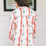 Woman with dark hair wearing a long-sleeve pajama top and pants set that features green, red, and pink bow graphics. 