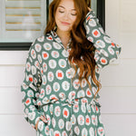 Woman with red hair wearing a long-sleeve top and long pant pajama set. The Pajamas feature fun red & green Christmas icon graphics. 