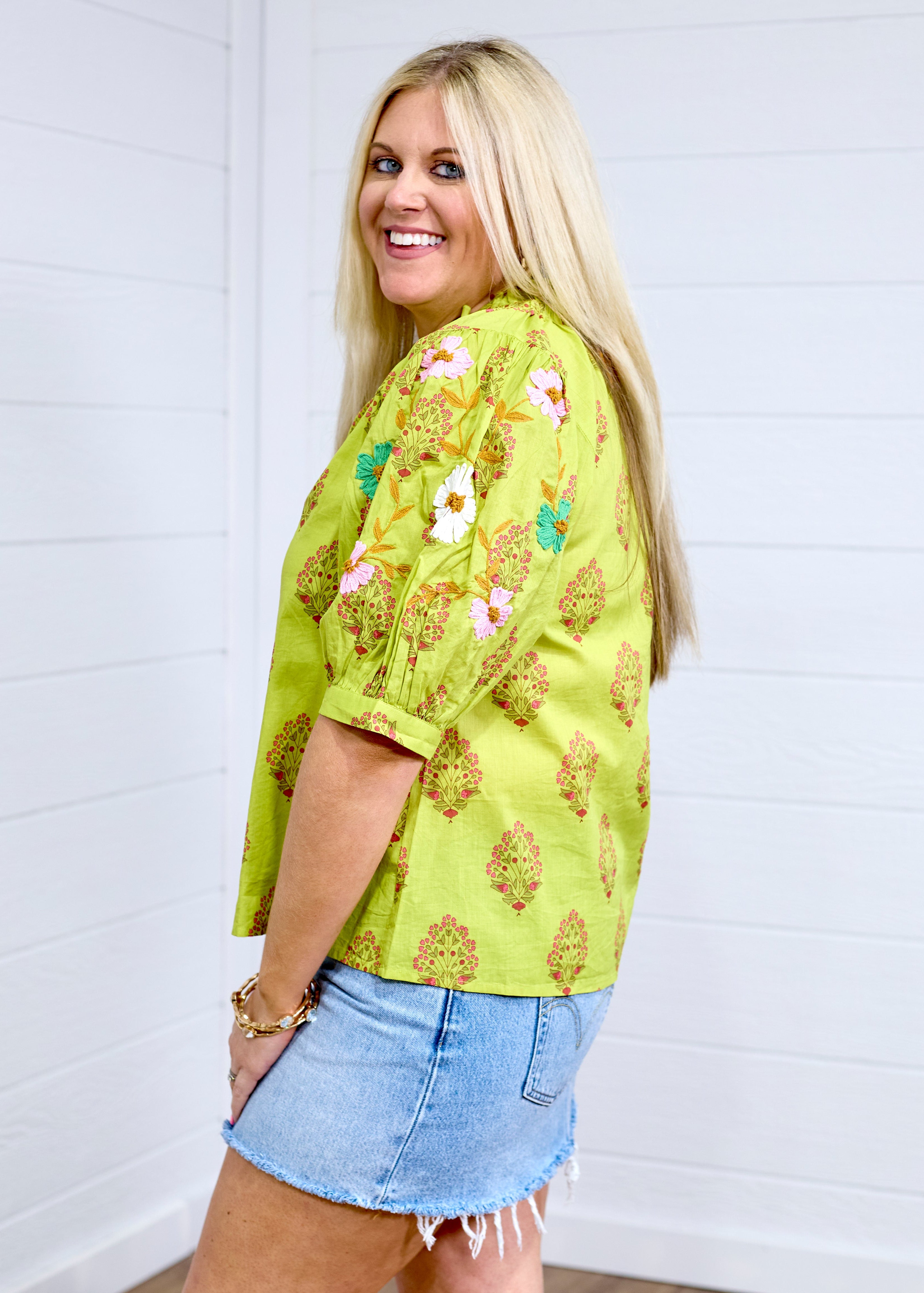 Woman with blonde hair shows side profile of the Margo Top with a white background. She has the top paired with a light-wash denim skirt.