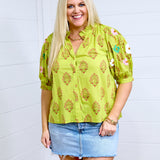 Woman with blonde hair in front profile wearing the Margo Top with a white background. She has the top paired with a light-wash denim skirt. 