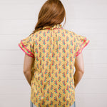 Women wearing a yellow top with floral print with ruffle sleeves and pink trim showing the back on a white background 
