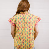 Women wearing a yellow top with floral print with ruffle sleeves and pink trim showing the back on a white background 
