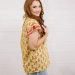 Women wearing a yellow top with floral print with ruffle sleeves and pink trim showing the side and sleeve on a white background 