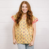 Women wearing a yellow top with floral print with ruffle sleeves and pink trim showing the front on a white background 
