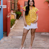 Women wearing a yellow top with floral print with ruffle sleeves and pink trim in a colorful atmosphere 