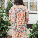 Woman with dark hair standing in a back profile position wearing the Nina Top in a lifestyle scene. The focal point of this image is the red/blue patchwork. The model paired this top with light-wash denim jeans.