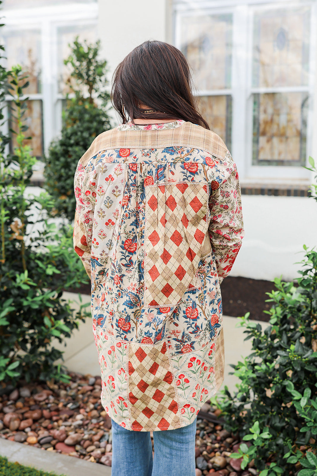 Woman with dark hair standing in a back profile position wearing the Nina Top in a lifestyle scene. The focal point of this image is the red/blue patchwork. The model paired this top with light-wash denim jeans.