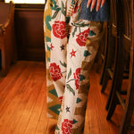 Woman with dark hair wearing the Pendleton Pants featuring stars embellishments, red rose graphics, and aztec print down side of pants. 