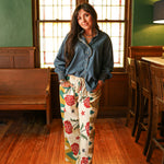 Woman with dark hair wearing the Pendleton Pants featuring stars embellishments, red rose graphics, and aztec print down side of pants. 