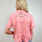 Back view women wearing a pink gingham pearl snap top with embroidered on back and ruffles at sleeves and waist. 
