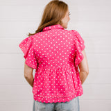 Woman wearing a pink polka dot blouse against a light background back view. 
