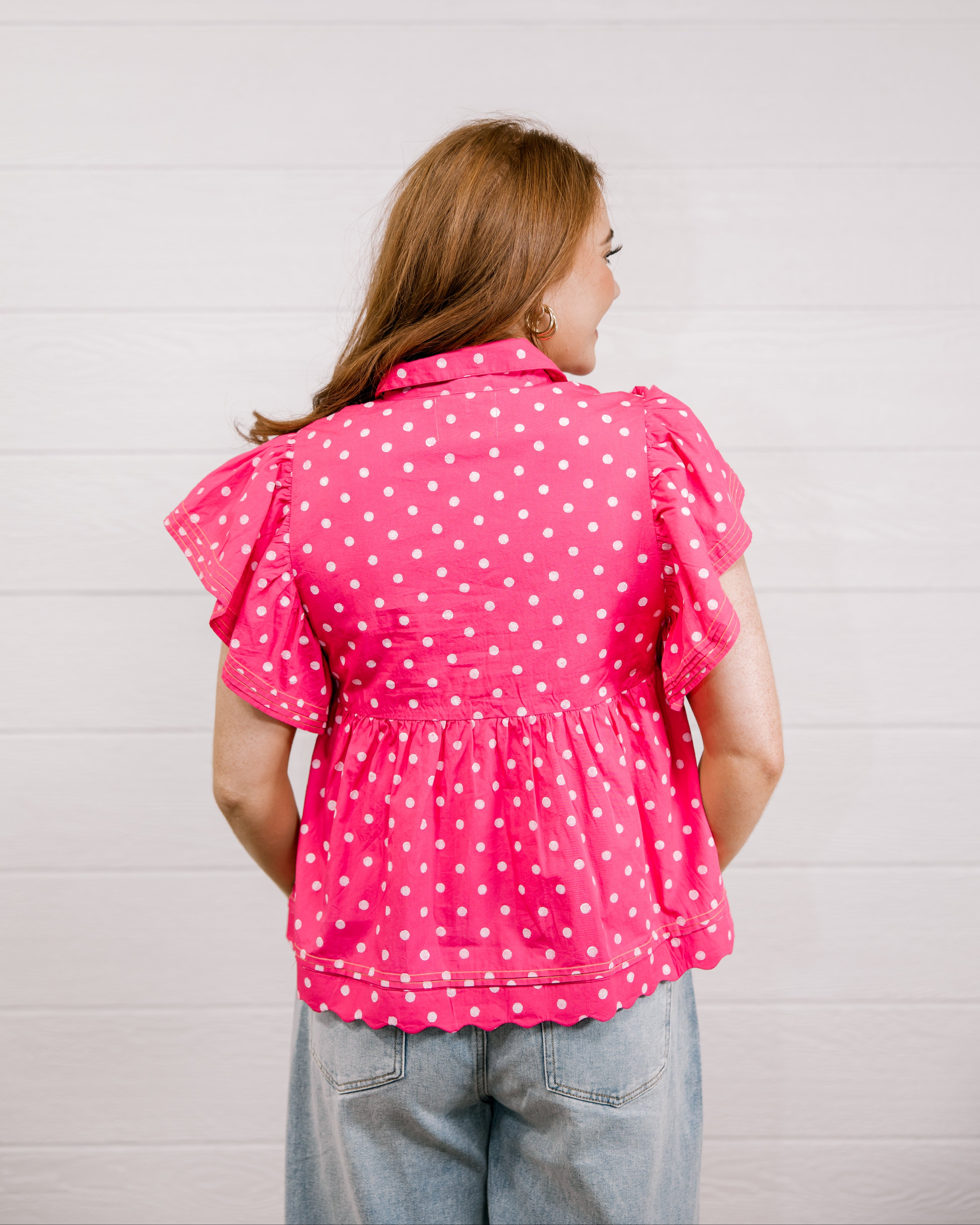 Woman wearing a pink polka dot blouse against a light background back view. 
