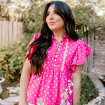 Pink top with white polk a dots and yellow accent stitching on women in a garden. 