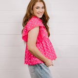 Woman wearing a pink polka dot blouse against a light background facing the side