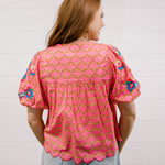 Woman wearing a pink patterned blouse against a plain background facing back. 