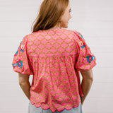 Woman wearing a pink patterned blouse against a plain background facing back. 