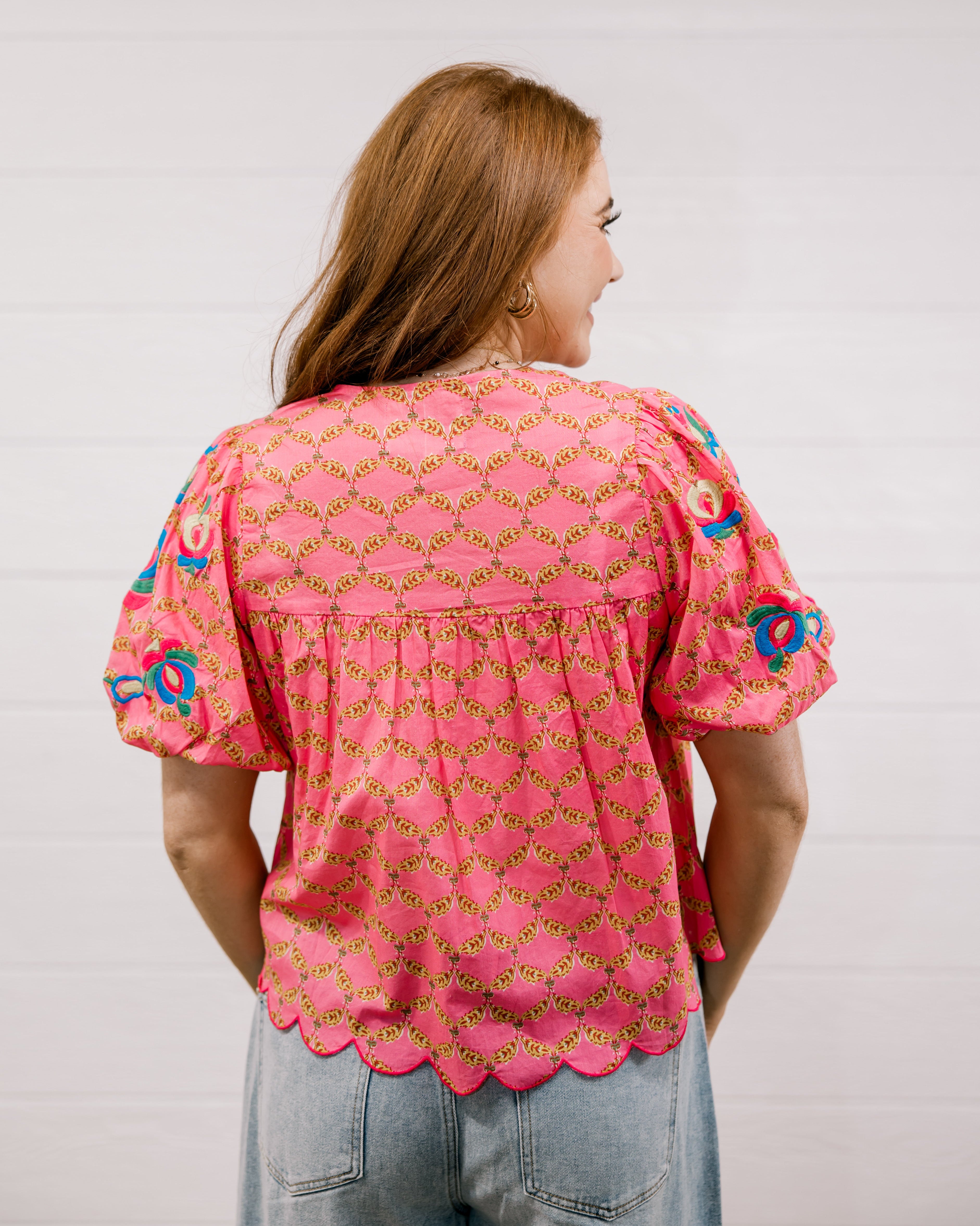 Woman wearing a pink patterned blouse against a plain background facing back. 
