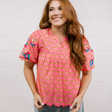 Woman wearing a pink floral blouse against a white background facing the front.