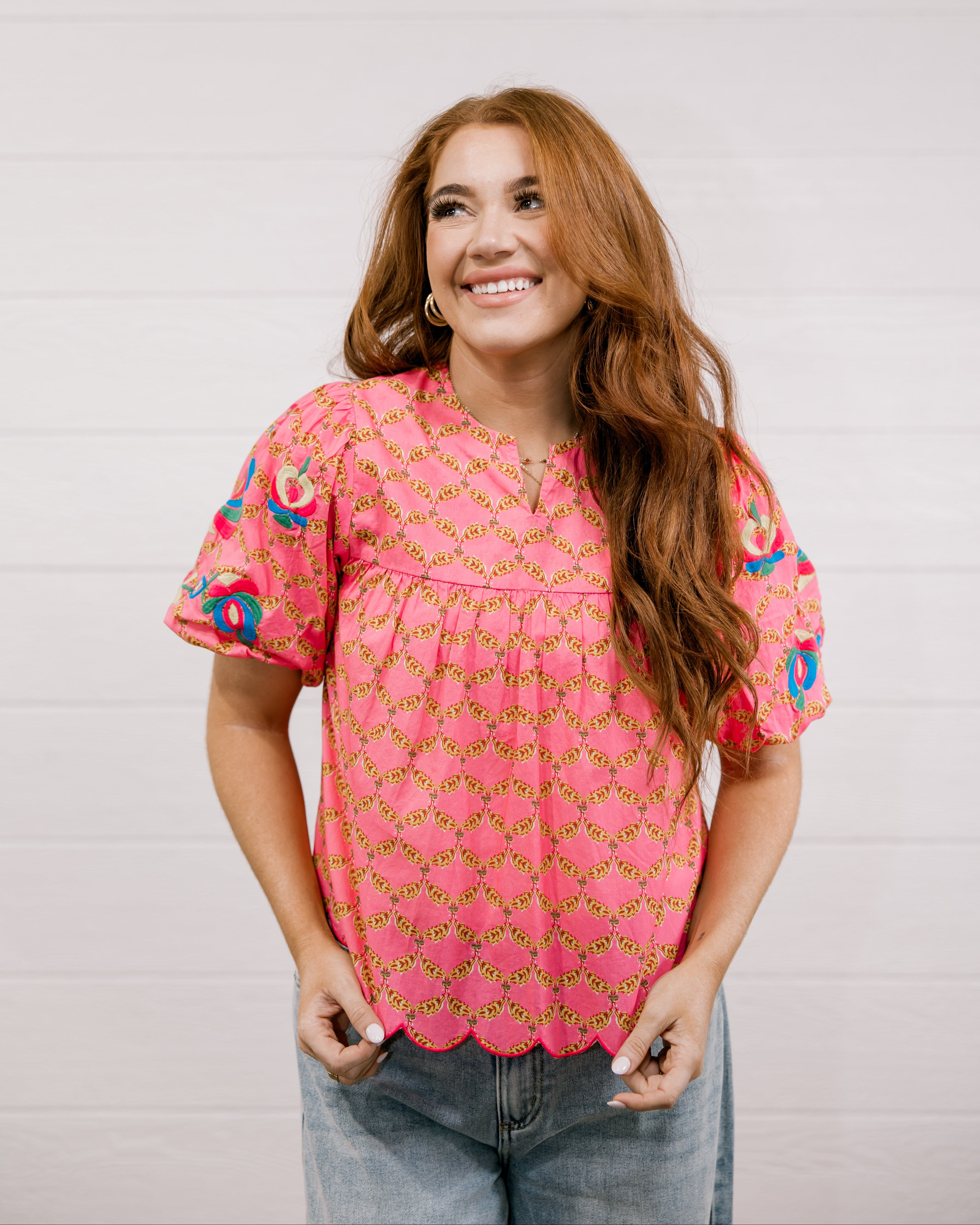 Woman wearing a pink floral blouse against a white background facing the front.