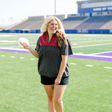 Woman with blonde hair standing in a front profile position wearing the Reece Top in a lifestyle scene. The focal point of this image is the red floral embroidery on front of top as well as v-neckline. The model paired this top with black denim shorts. 