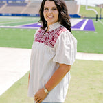 Woman with dark hair standing in a side profile position wearing the Reece Top in a lifestyle scene. The focal point of this image is the embroidery on chest as well as sleeve length and top length The model paired this top with light-wash denim shorts. 
