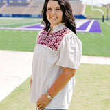 Woman with dark hair standing in a side profile position wearing the Reece Top in a lifestyle scene. The focal point of this image is the embroidery on chest as well as sleeve length and top length The model paired this top with light-wash denim shorts. 